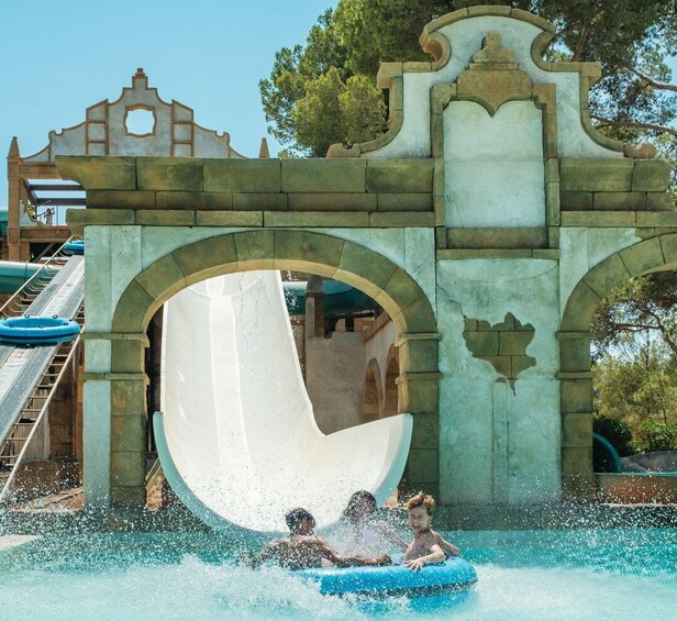 A water slide with a large archway, water splashing, and people in inflatable tubes. 4