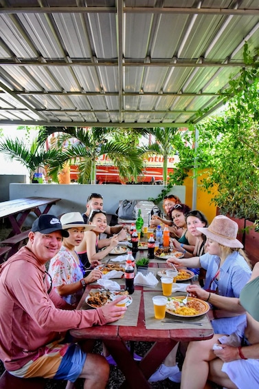 A group of people sitting at a picnic table outdoors, eating food and drinking beverages. 3