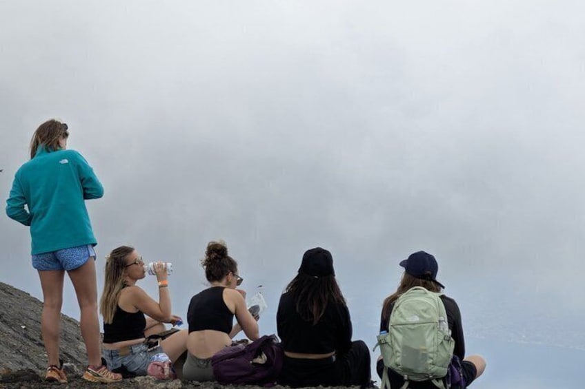 Un grupo de personas sentadas y de pie sobre un afloramiento rocoso, con vistas a un paisaje nublado. 2