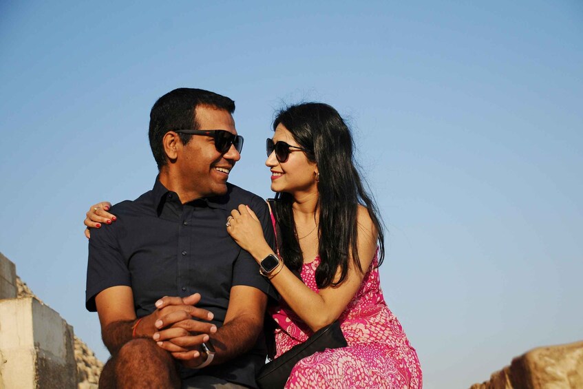 A couple sitting on a stone structure with a clear sky in the background. 4