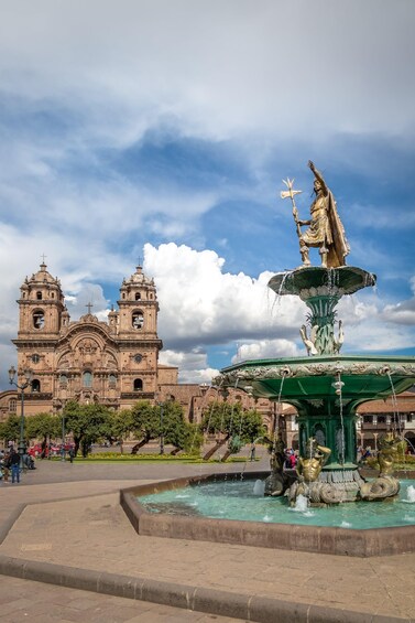 A large cathedral with two towers and a statue of a figure holding a staff in front of it. 1
