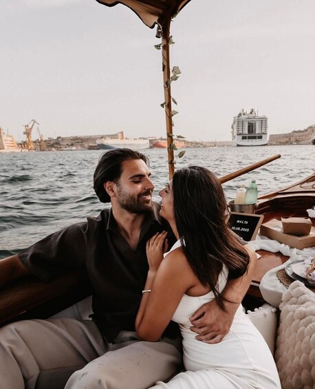 A couple on a boat with a cityscape and a ship in the background. 5