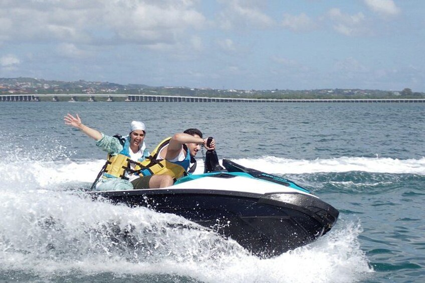 A person jet-skiing on a body of water with a bridge in the background. 1