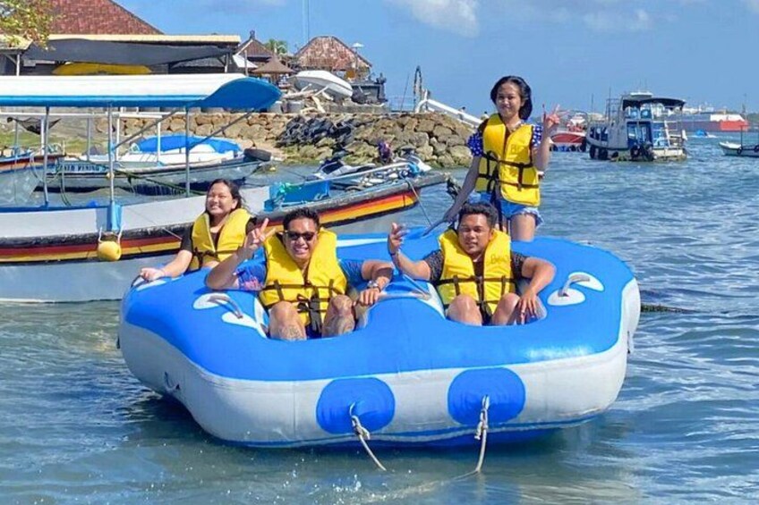 A group of people on a blue inflatable raft in a marina with boats and docks in the background. 3