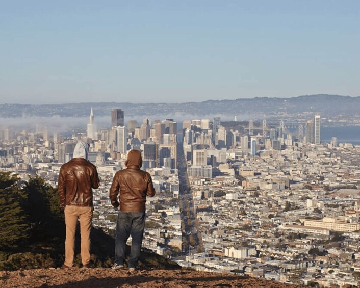 Two people standing on a hill overlooking a cityscape with numerous buildings and a clear sky. 5