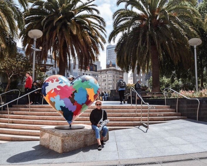 A colorful heart-shaped sculpture in a public square with palm trees and steps leading up to it. 4