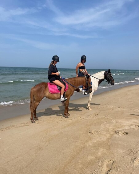 Two people riding horses on a beach with the ocean in the background. 1