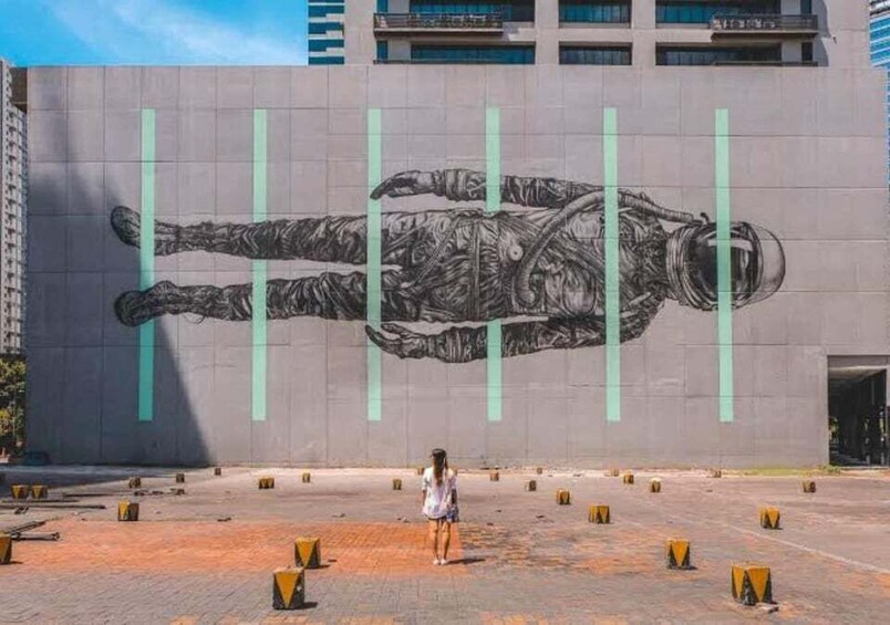 A mural of a person lying down on a building wall, with a person standing in front of it. 1
