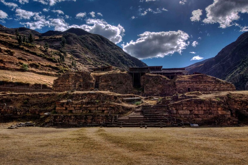 A historical stone structure with a staircase leading up to a platform, surrounded by mountainous terrain. 3