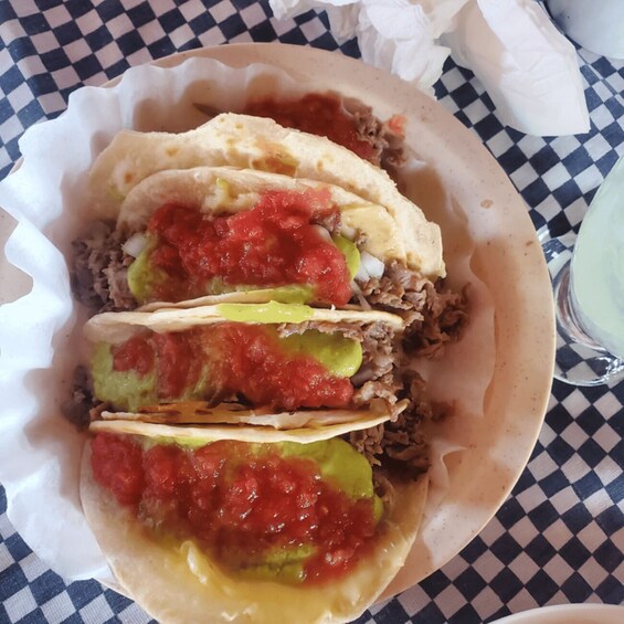 Three tacos with meat, guacamole, and salsa in a paper container. 1