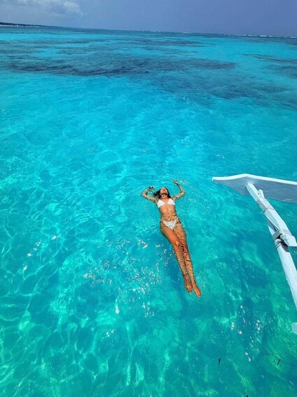 A person floating in clear turquoise water with a boat in the background. 3