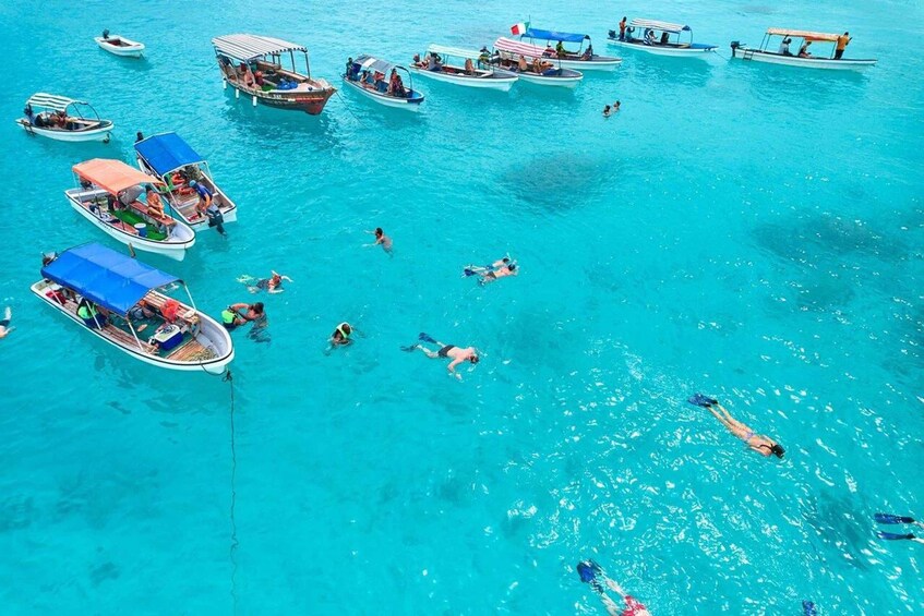 A turquoise sea with several boats, some with canopies, and people swimming and snorkeling. 1
