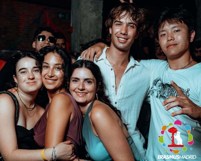 A group of people at an indoor event with a logo that reads 'ERASMUSMADRID' on the wall. 1
