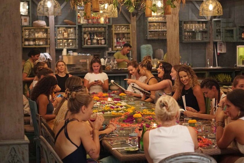 A group of people dining at a restaurant with a rustic interior, wooden tables, and hanging plants. 1