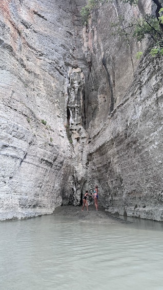 A rocky cliff with a cave entrance and two people standing at the base. 2