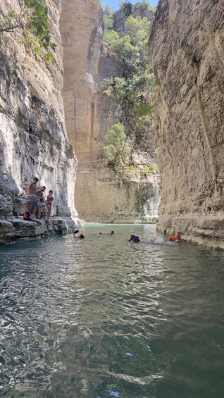 A canyon with a clear water body, rocky cliffs, and people swimming. 2