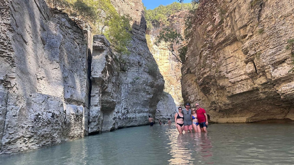 A group of people standing in a narrow canyon with steep rock walls and a small stream. 5