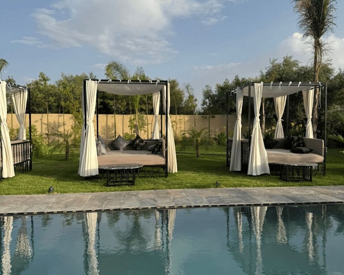 A poolside area with two white canopies and cushioned seating. 1