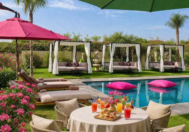 A poolside setting with lounge chairs, a table with drinks and snacks, and a pergola with a canopy. 1