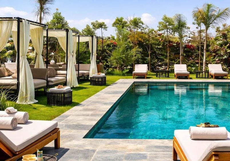 A poolside with lounge chairs, a canopy, and a tropical garden. 2