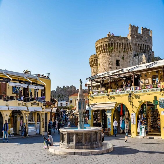 A bustling square with a historic castle in the background, surrounded by various shops and restaurants. 1