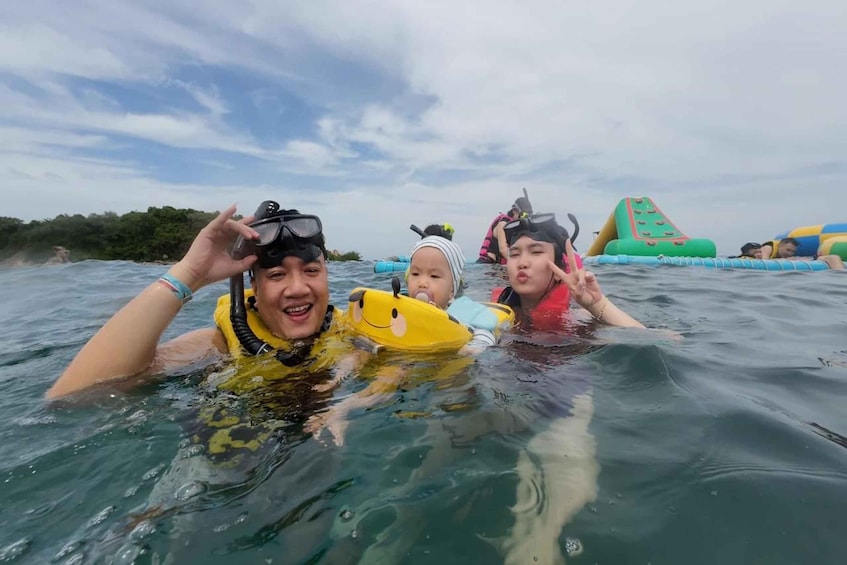 Three people in water with life vests, a baby in a yellow float, and inflatable structures in the background. 1