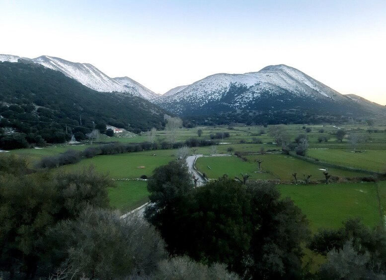 A valley with green fields, a winding road, and snow-capped mountains in the background. 3