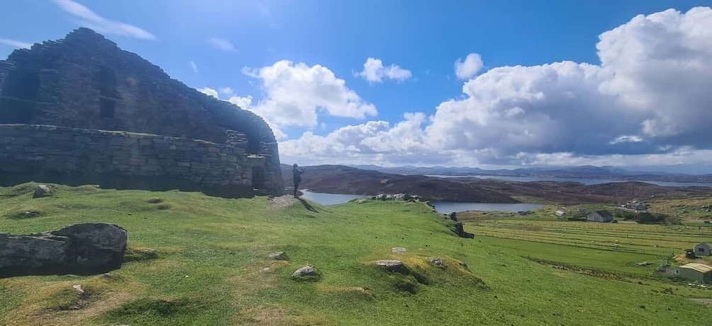A grassy landscape with a large rock formation, a body of water, and distant hills. 3