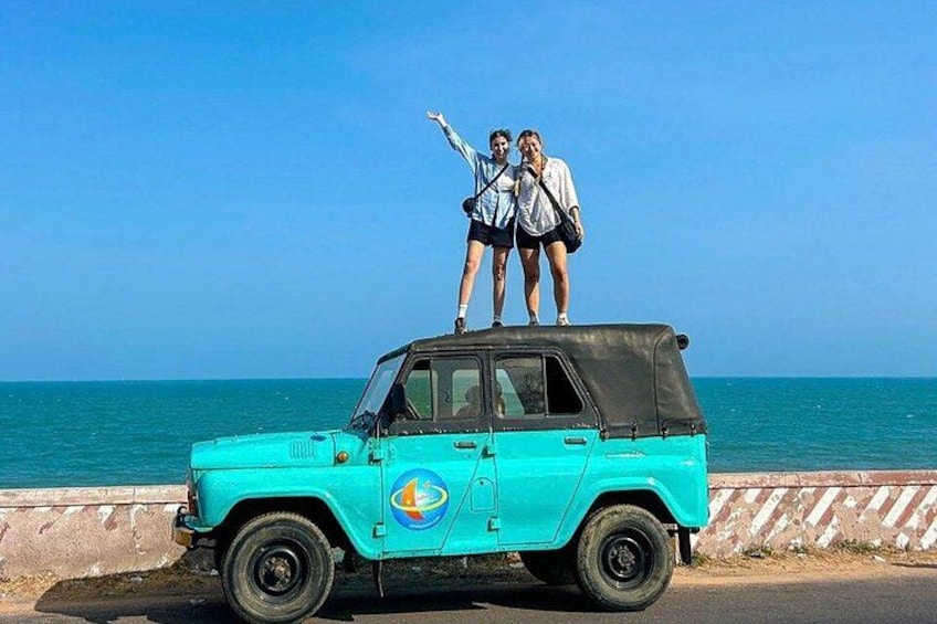 Een turquoise terreinwagen geparkeerd aan de kust, met twee personen op het dak. 1