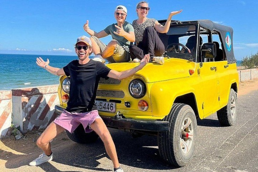 Een gele auto geparkeerd aan de kust, met drie mensen op de foto. 3