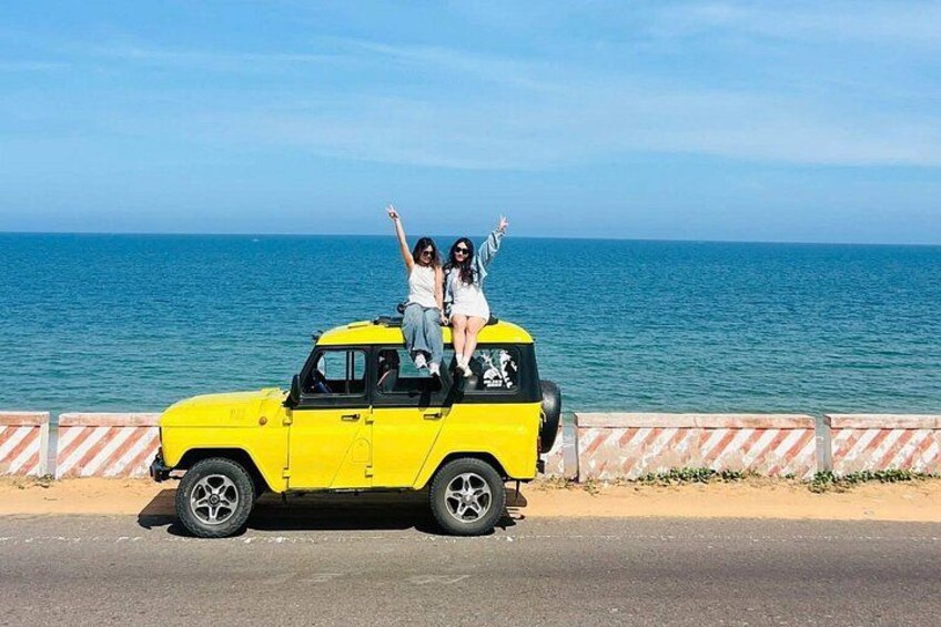 Een gele auto met twee personen erop, geparkeerd aan de kust. 5