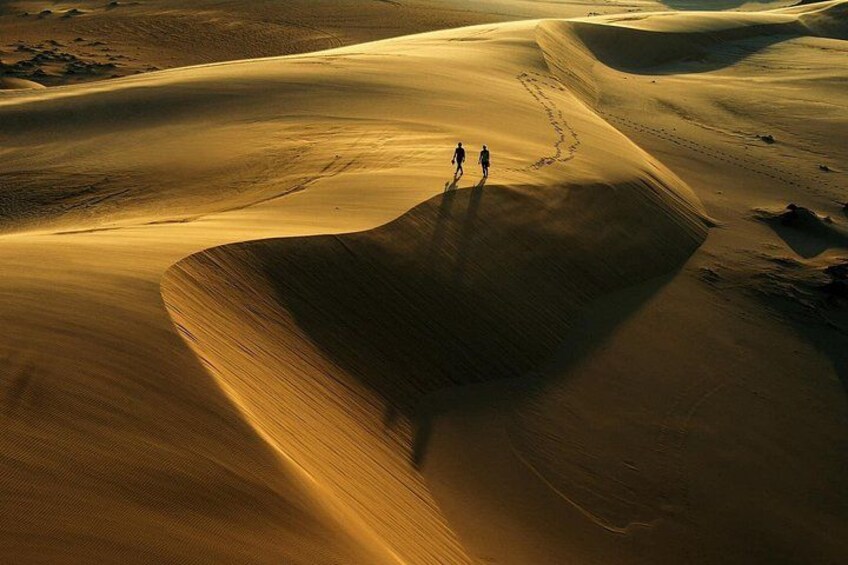 Woestijnlandschap met zandduinen en twee personen die over een duin lopen. 2