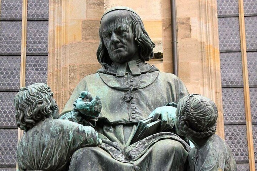 Een standbeeld van een zittende figuur met een boek, omringd door twee kleinere figuren. 5