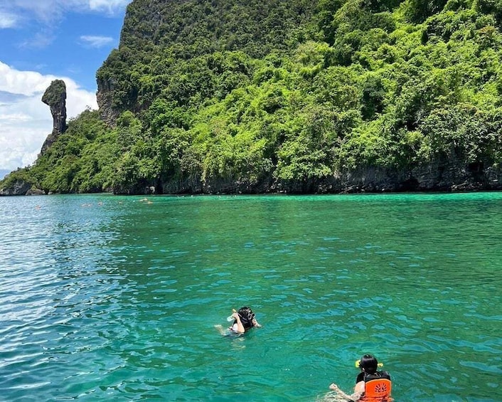 A person swimming in clear turquoise water with a mountainous backdrop. 2