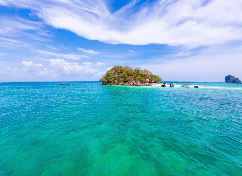 A turquoise sea with a small island covered in greenery, boats in the water, and a clear sky. 3