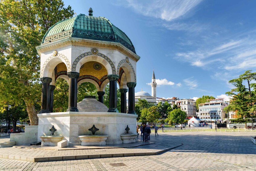 A historical pavilion with a green dome and arches, surrounded by trees and buildings in the background. 2
