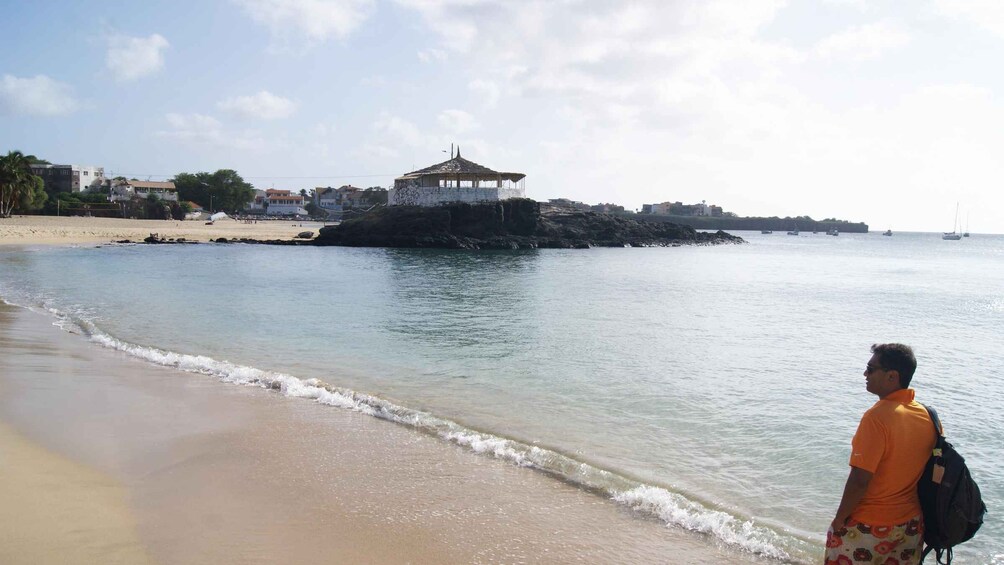 A beach with waves, a person in orange, and a building on a rocky outcrop. 4