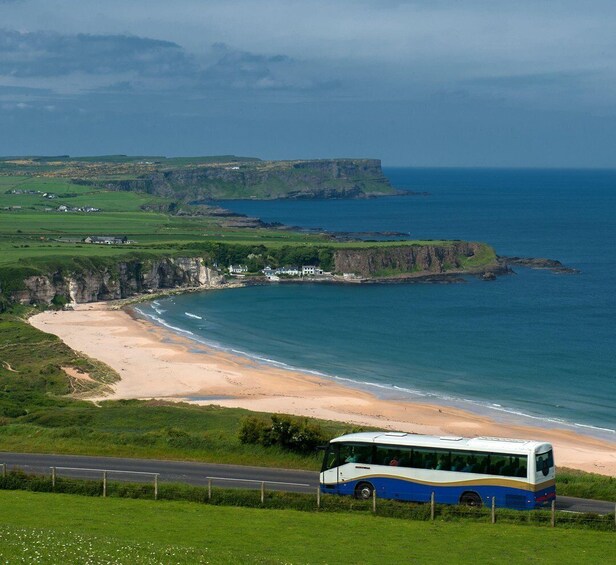 A coastal landscape with cliffs, a beach, and a bus on the road. 4