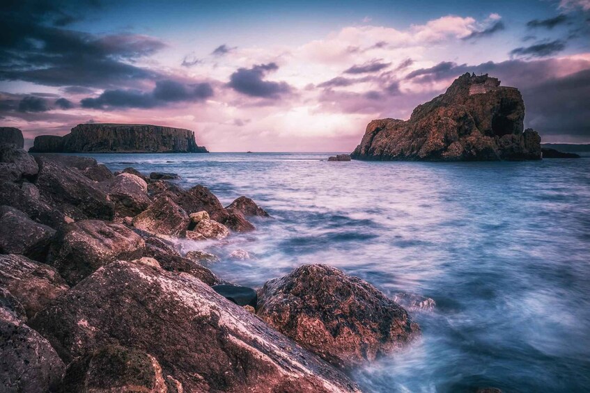 A rocky coastline with large boulders and cliffs under a twilight sky. 2