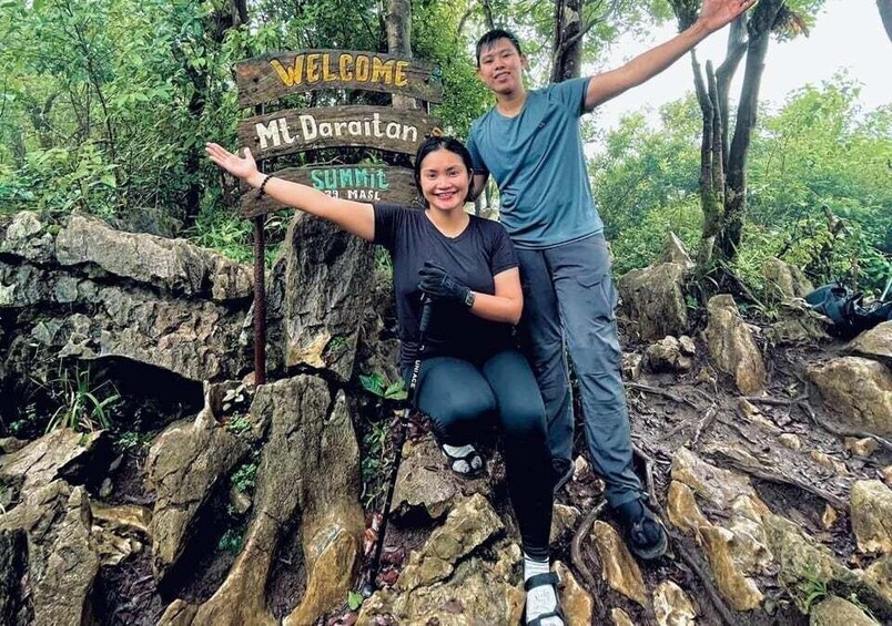 Two people posing in front of a wooden sign with 'Welcome Mt Daraitan' and 'Summit Masai' written on it. 2