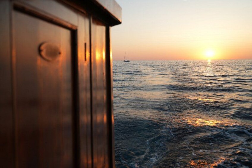 A wooden structure, possibly a cabin, overlooking a calm sea at sunset with a sailboat in the distance. 3