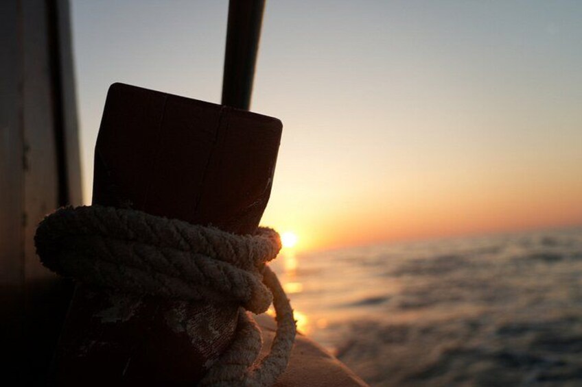 A sunset over the ocean with a rope and a book on a surface. 2