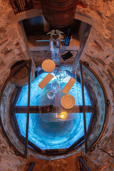 A circular stone structure with a glass enclosure, containing a blue-lit interior and various objects like plates and bottles. 5