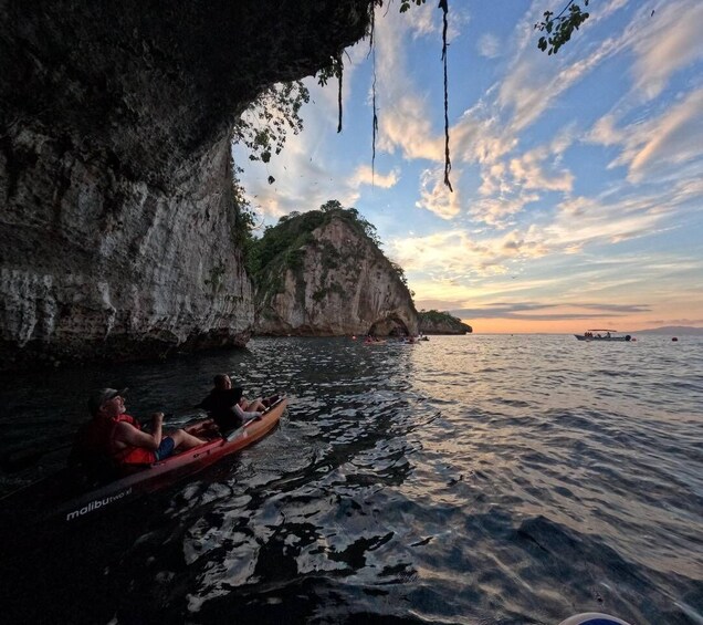 A boat with two people on a calm sea, a rocky cliff, and a sunset in the background. 4