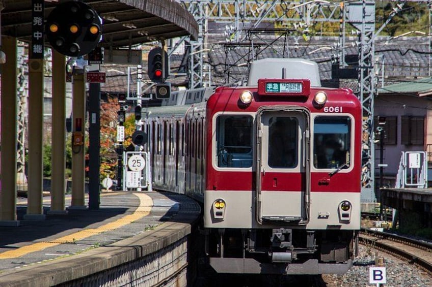A red and white train at a station platform with overhead electrical lines and a pedestrian crossing. 1