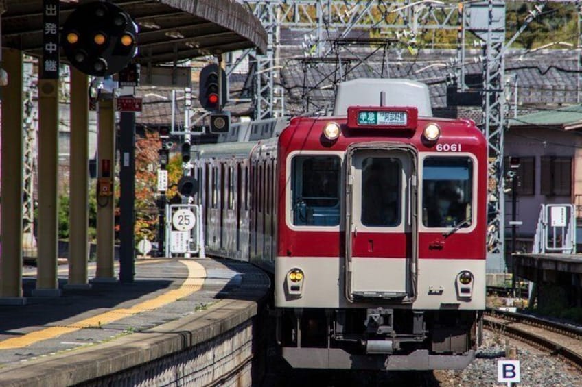 A red and white train at a station platform with overhead electrical lines and a traffic light. 5