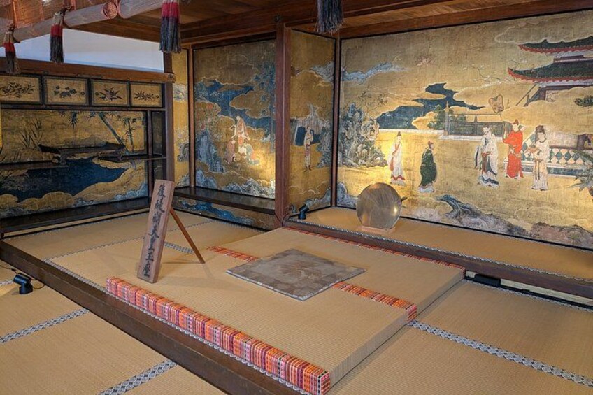A traditional Japanese room with tatami flooring, a hanging scroll, and a painting of historical figures. 5