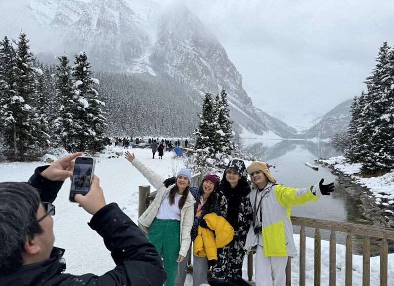 A group of people taking a selfie by a snow-covered lake with mountains in the background. 4