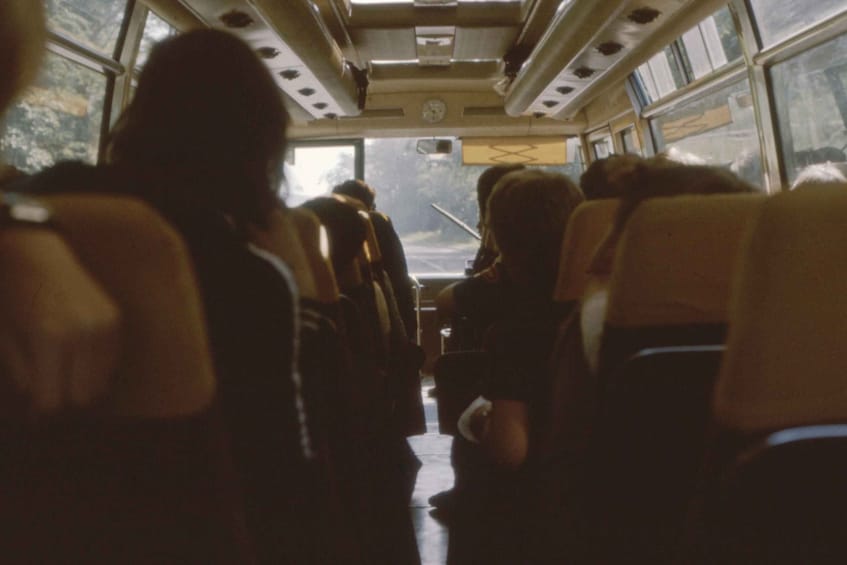 The interior of a bus with passengers seated and facing forward. 1