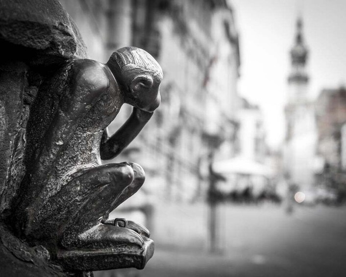 A sculpture of a praying figure on a stone ledge, with a blurred cityscape in the background. 4